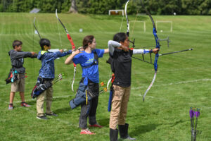 Four kids lined up on the shooting line with bows at the ready.